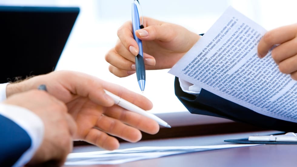 Two sets of hands holding pens and paper over a table during a business meeting.