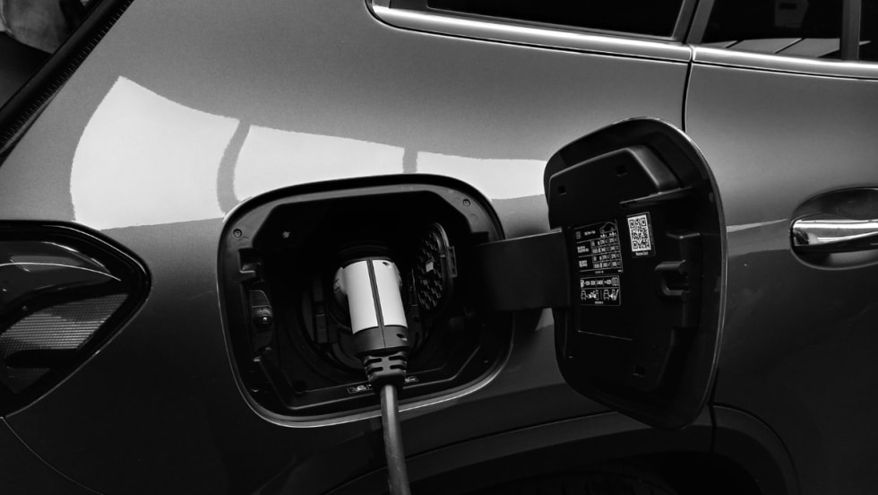 The open charging port of a gray electric vehicle with a charging cable attached.