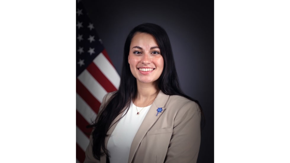 Smiling professional woman in beige blazer standing in front of American flag