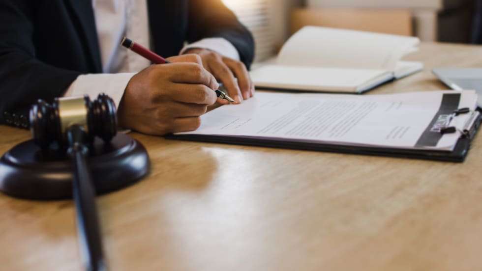 hand signing paperwork on a clipboard on top of a desk with a gavel to the side