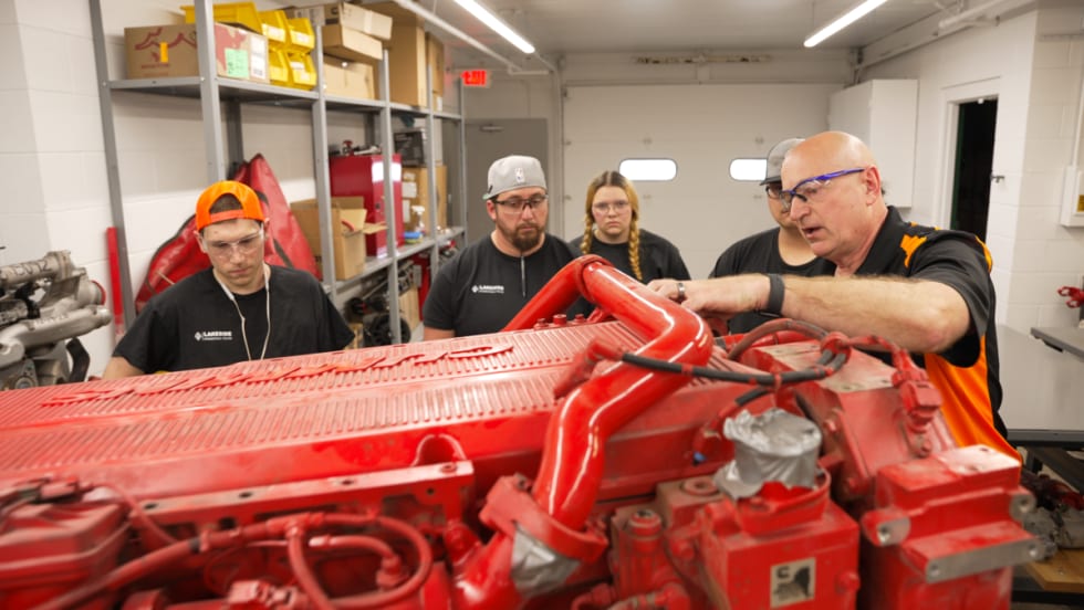Instructor speaking to students surrounding a red piece of diesel equipment.