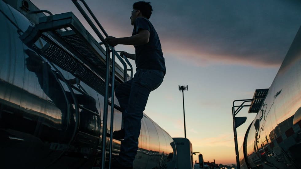 Truck driver climbs side of tanker trailer at sunset or sunrise