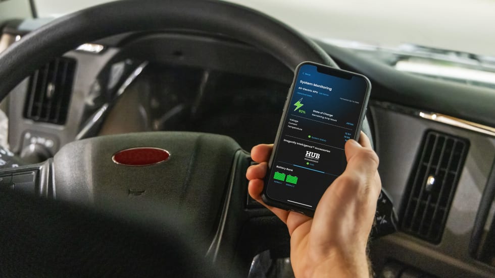 Truck driver holding phone in hand with Battle Born app monitoring lithium batteries.
