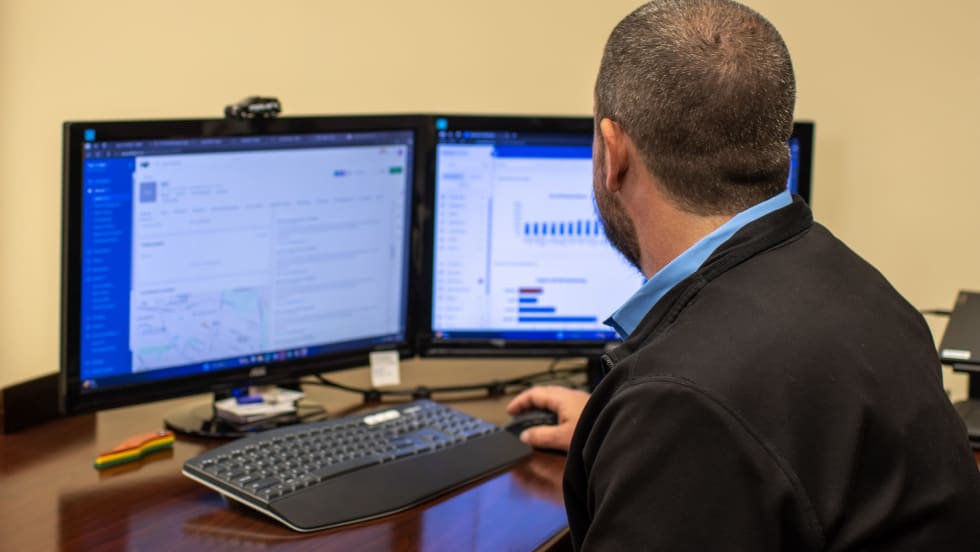 Fleet manager reviews maintenance and performance data on dual computer monitors.