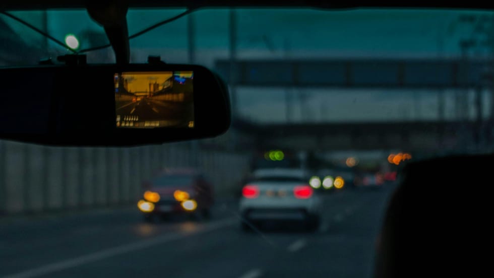 Looking through the windshield of a car from the interior, a dashcam is connected to the rearview mirror.