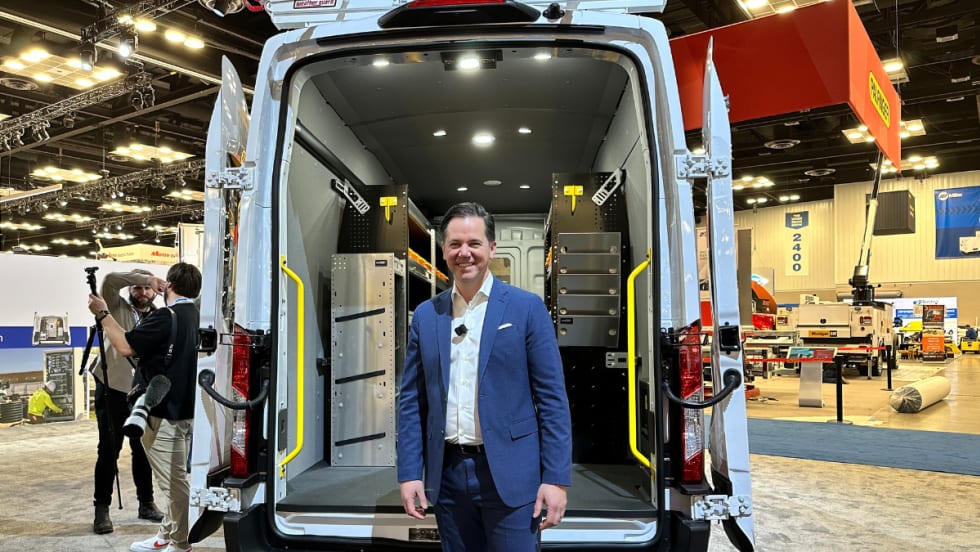 Matt Atkenson poses with an upfitted van on a show floor. 