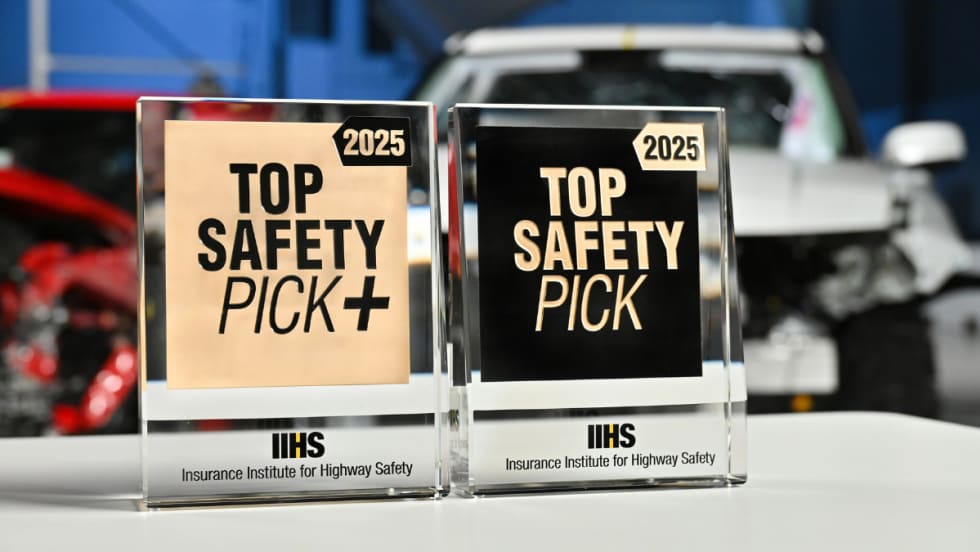 Close up image of Top Safety Pick+ and Top Safety Pick awards in front of crash test cars.