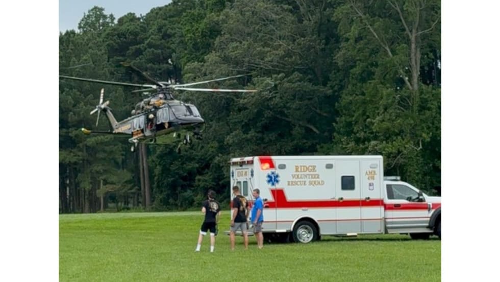 Medical helicopter landed on grassy field near ambulance with people nearby