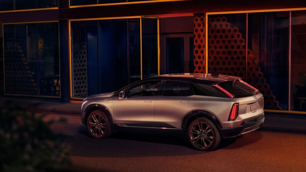 The back and side of a silver SUV at night, parked in front of a building.
