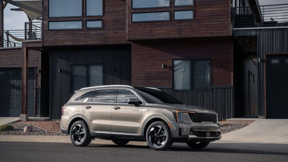 A tan and black Kia SUV parked on the street in front of a modernized brick house.