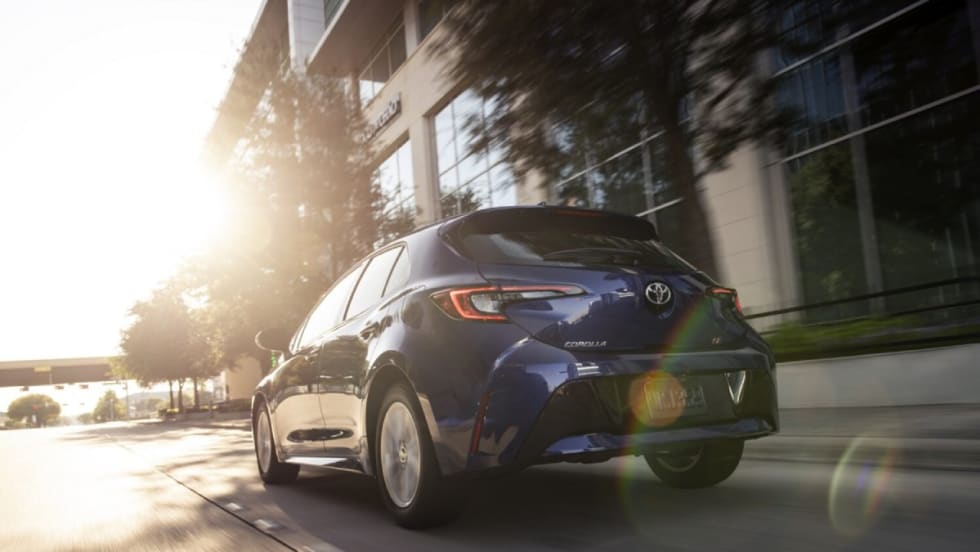 An action shot of a blue 2025 Toyota Corolla Hatchback driving down a city street.
