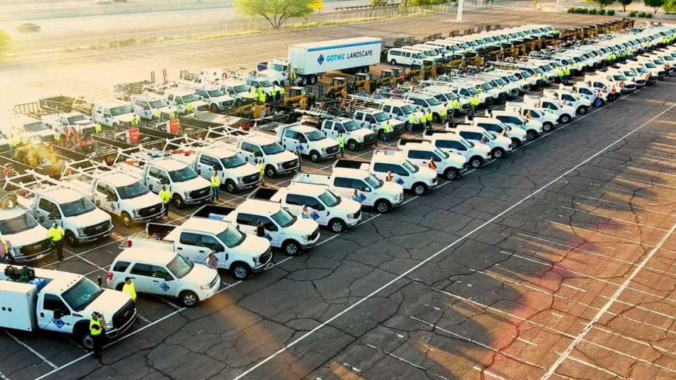 A large group of Gothic Landscape fleet vehicles and personnel pose in a parking lot.