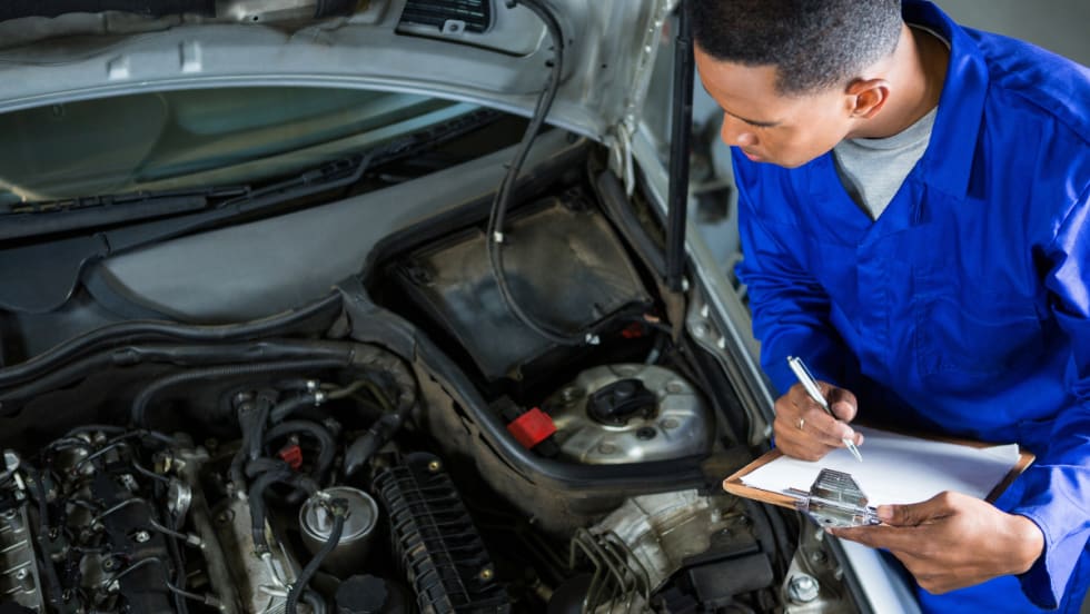 mechanic filling out clipboard while inspecting under hood of vehicle