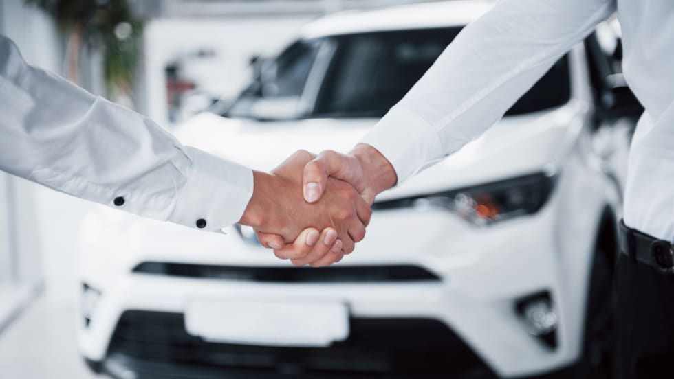 two people shaking hands in front of a new car that says Smarter Deals Ahead 