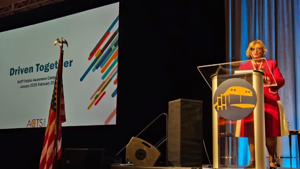 Molly McGee Hewitt stands at a podium on a stage with a screen behind her that says "Driven Together" and the NAPT logo