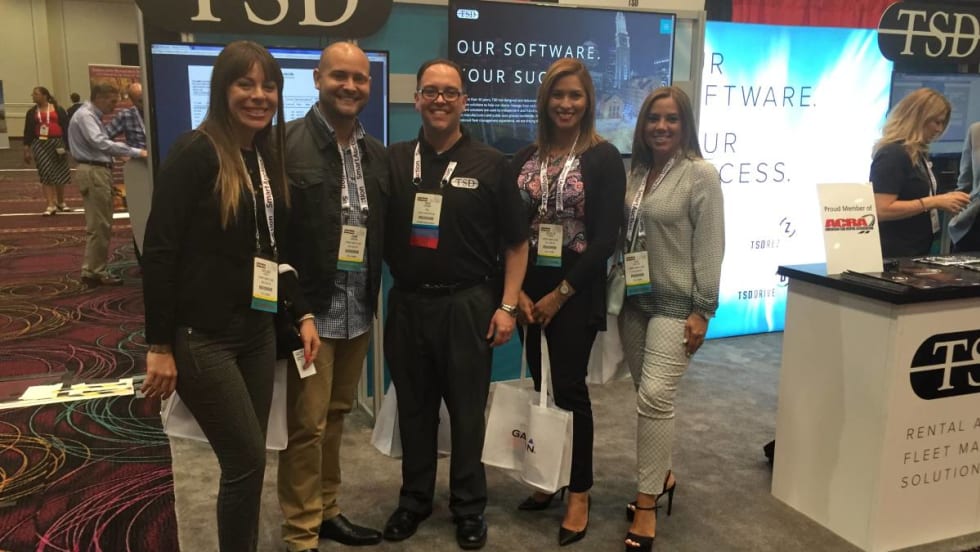 Five trade show attendees lined up in front of an exhibit booth.