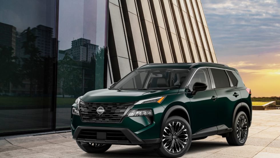 Dark colored Nissan SUV parked in front of modern glass and stone buildings at sunset.