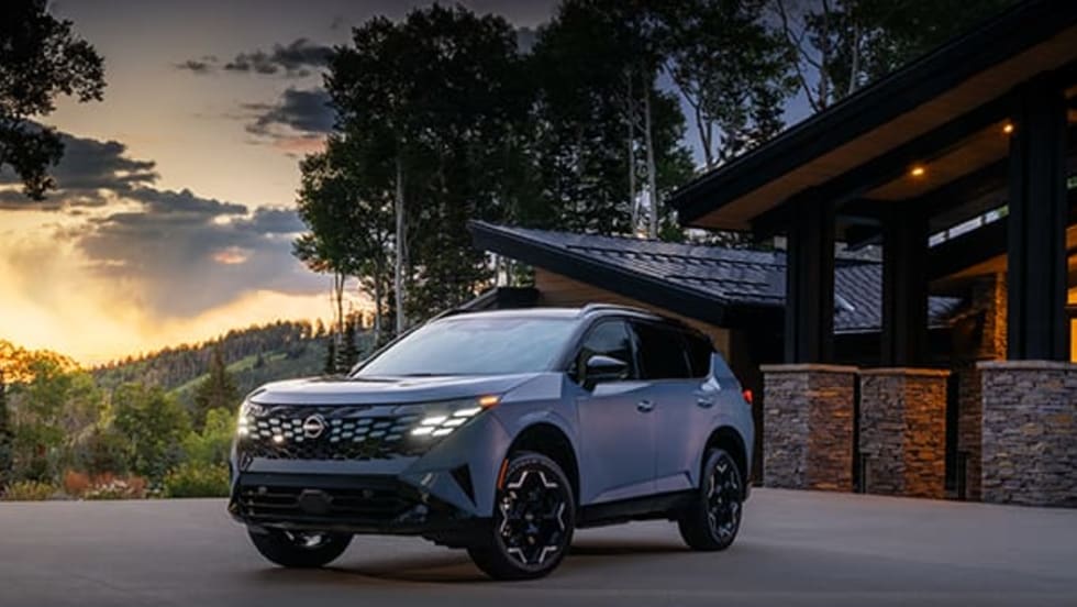 A grey Nissan drives on a road at sunset