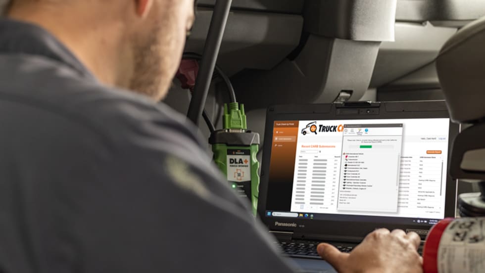 Technician using Truck Check-Up diagnostic software on a Panasonic Toughbook laptop inside a truck cab