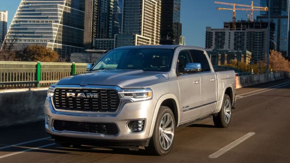 An image of a silver 2025 Ram 1500 pickup truck driving on a city road with skyscrapers and construction in the background.