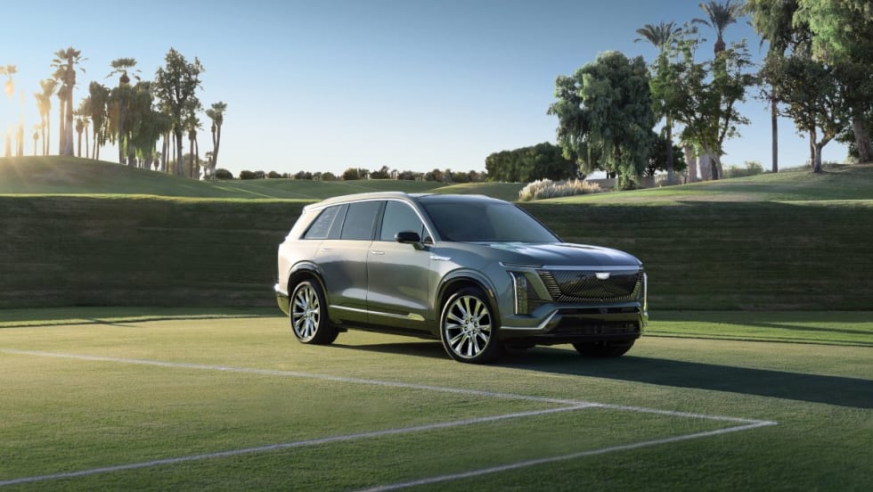 A pale green 2026 Cadillac Vistiq parked on a tennis court with palm trees and a blue sky in the background.
