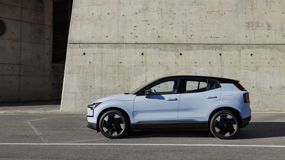The left side view of a cloud blue 2025 Volvo EX30 parking in front of a gray concreate wall.