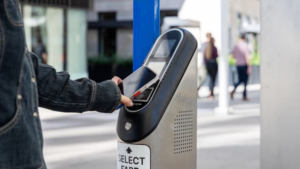 Someone taps their phone to a bus or rail validator to pay to ride via mobile wallet.