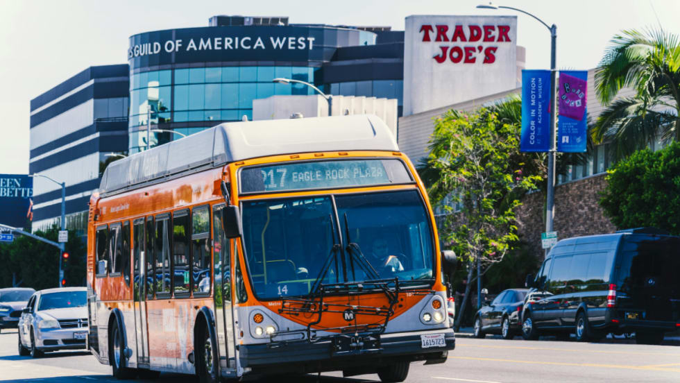 An orange LA Metro bus driving on a city street.