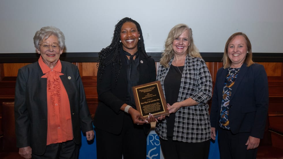 Four women pose for a group photos with the New Flyer award plaque.