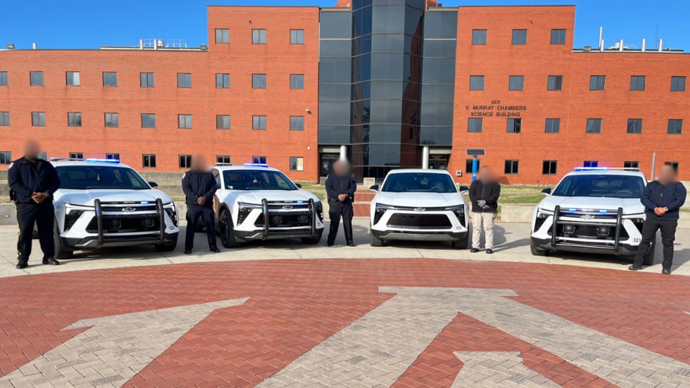 Five Alabama A&M police officers pose with four electric patrol SUVs on campus in front of a brick academic building.