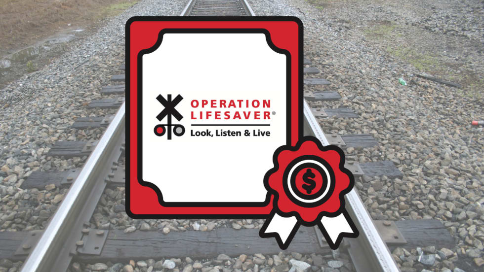 Operation Lifesaver rail safety grant graphic displayed over railroad tracks, highlighting federal funding for crossing safety and trespass prevention campaigns.