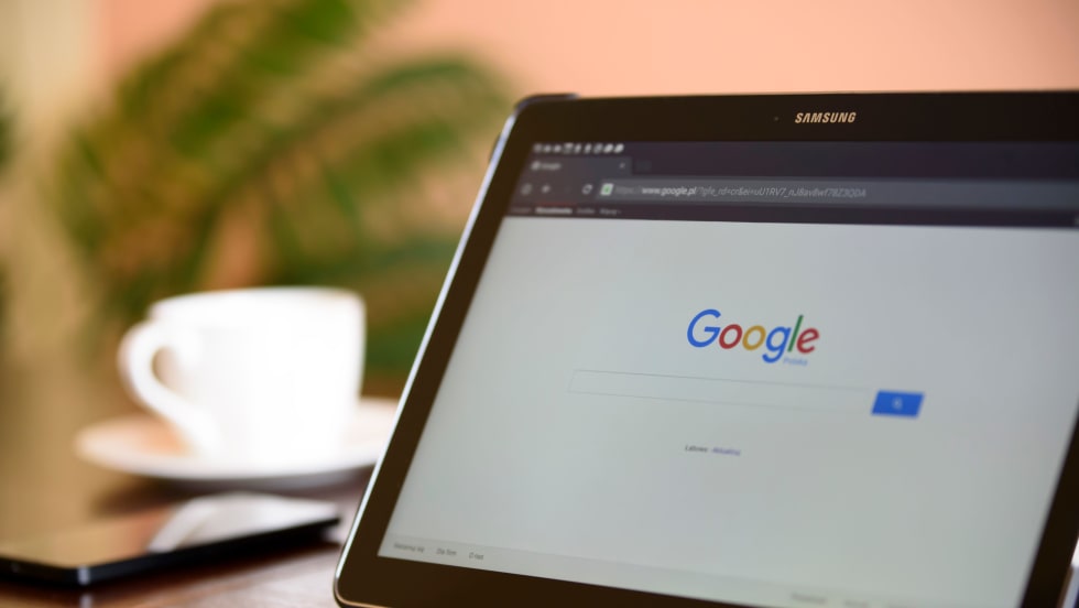 Photo of digital tablet sitting on surface with a Google webpage on screen and a coffee cup beside it