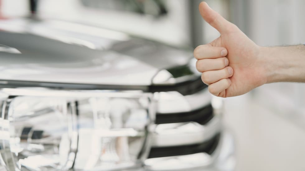car in background with hand giving a thumbs up in front