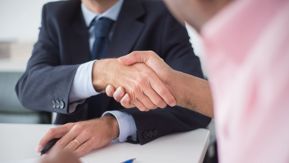 Photo of a man in a suit shaking hands with a man across a desk