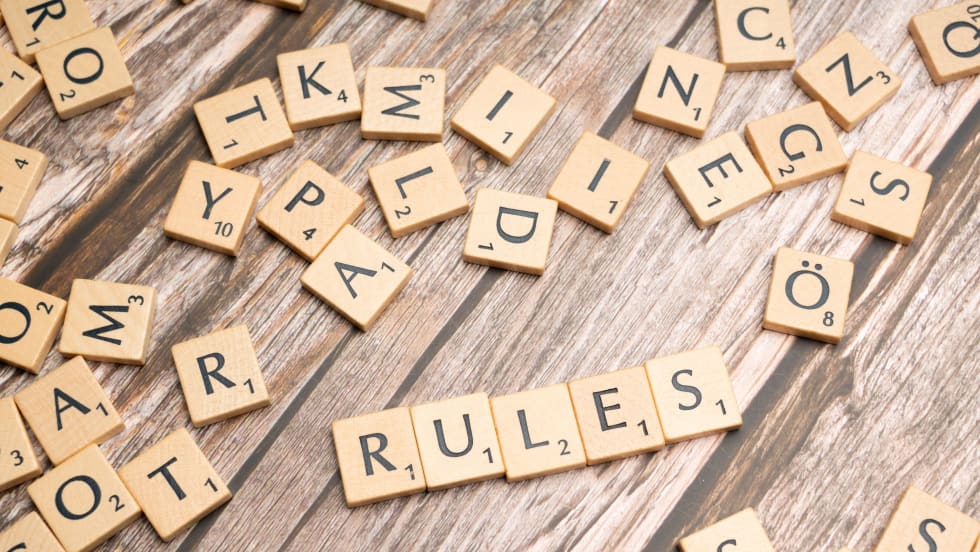 Scrabble tiles  spelling out 'Rules' among random letter tiles, all on a wooden surface