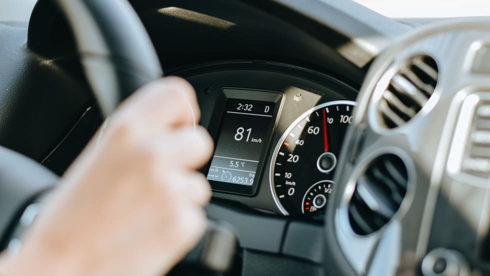 Photo of a woman's hand gripping a steering wheel with the dashboard display in the background