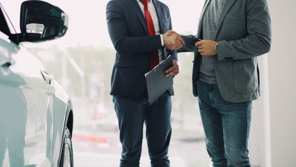 two men in suits shaking hands next to a white car