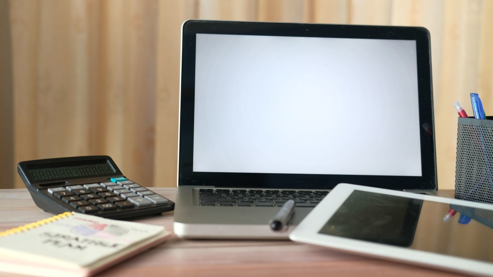 Laptop computer, tablet, calculator and notebook on a desk