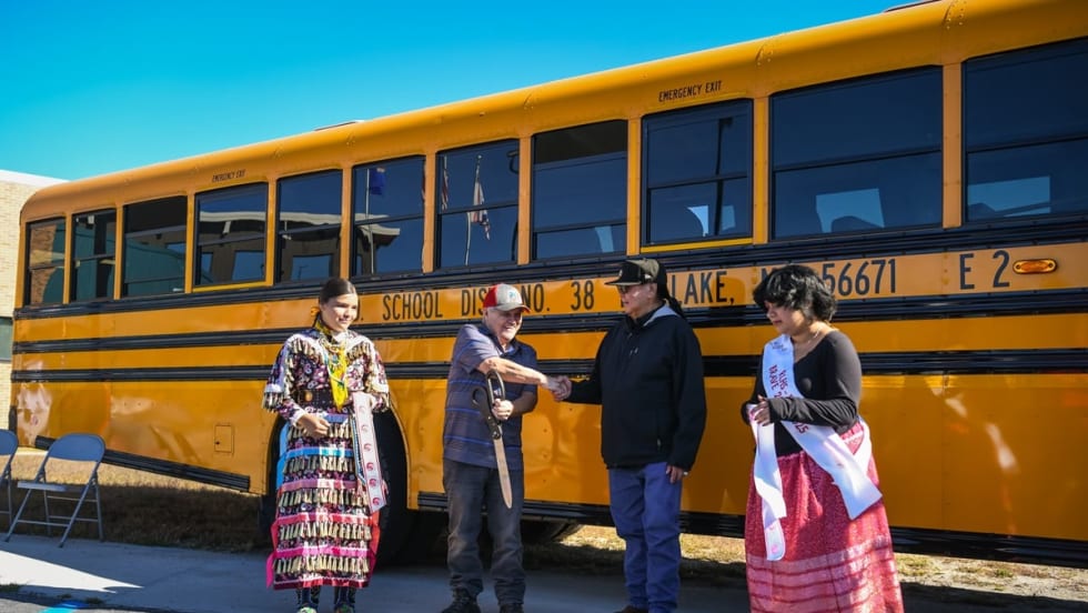 three people cut a ribbon in front of a school bus