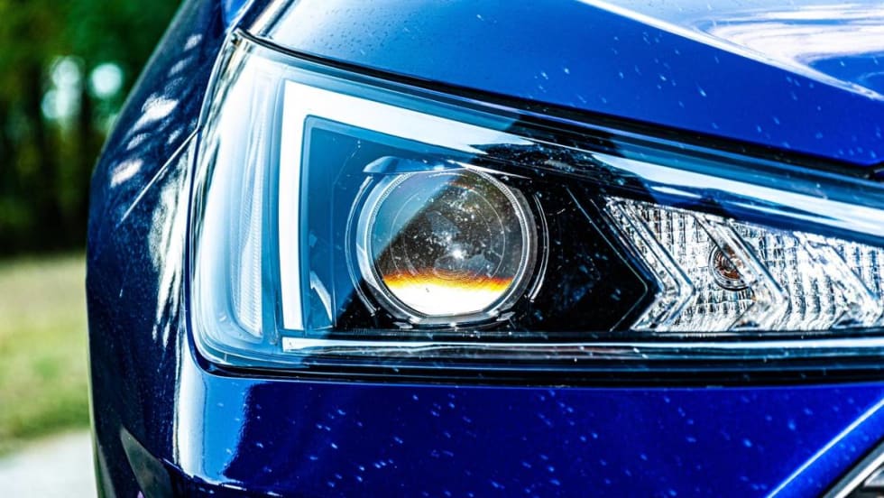 Close up of a blue car’s headlight with white marks or scratches on the surrounding auto body.
