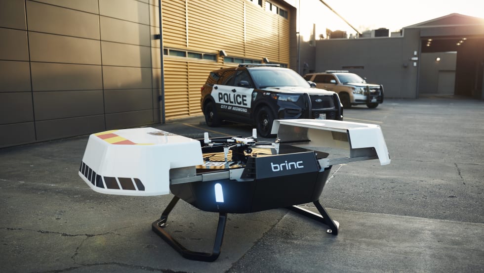 A Responder drone sits atop a Responder Station charging nest with two law enforcement vehicles in the background.