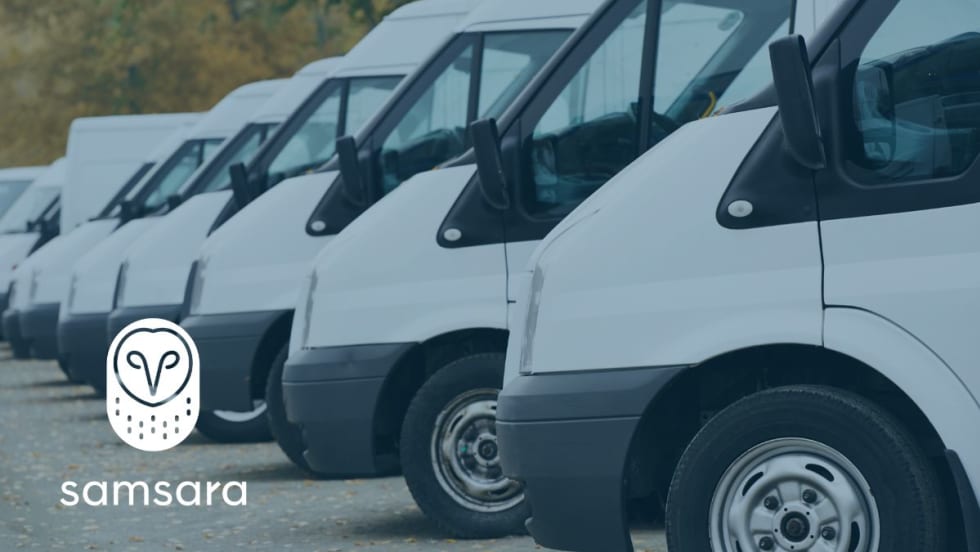 A line of parked cargo vans and the Samsara logo. 