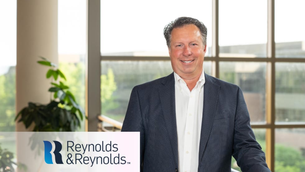 Scott Worthington, vice president of product management at Reynolds and Reynolds, stands indoors in front of large windows wearing a navy blazer and white shirt.