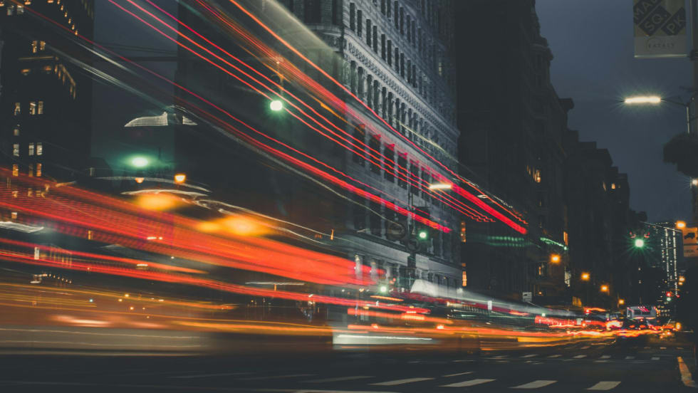A long exposure image in New York at night, the light trails of cars stream across the frame.