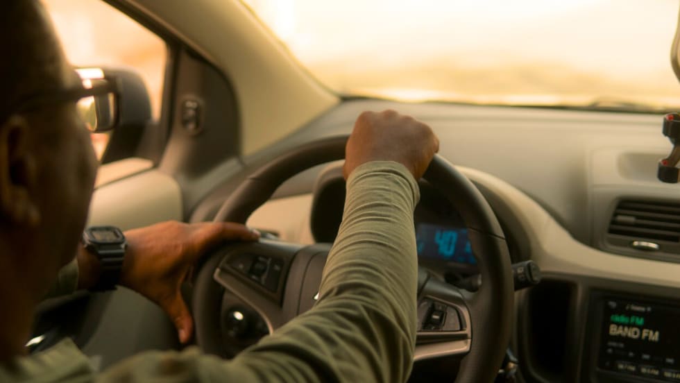 From the interior of a car, a man in a green long sleeve shirt is driving.