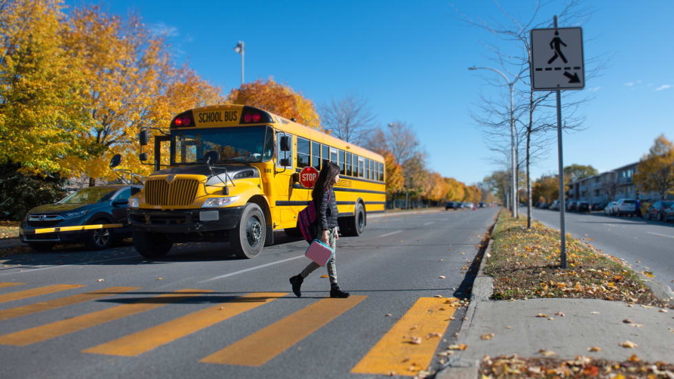 A student crosses the street in front of a school bus.