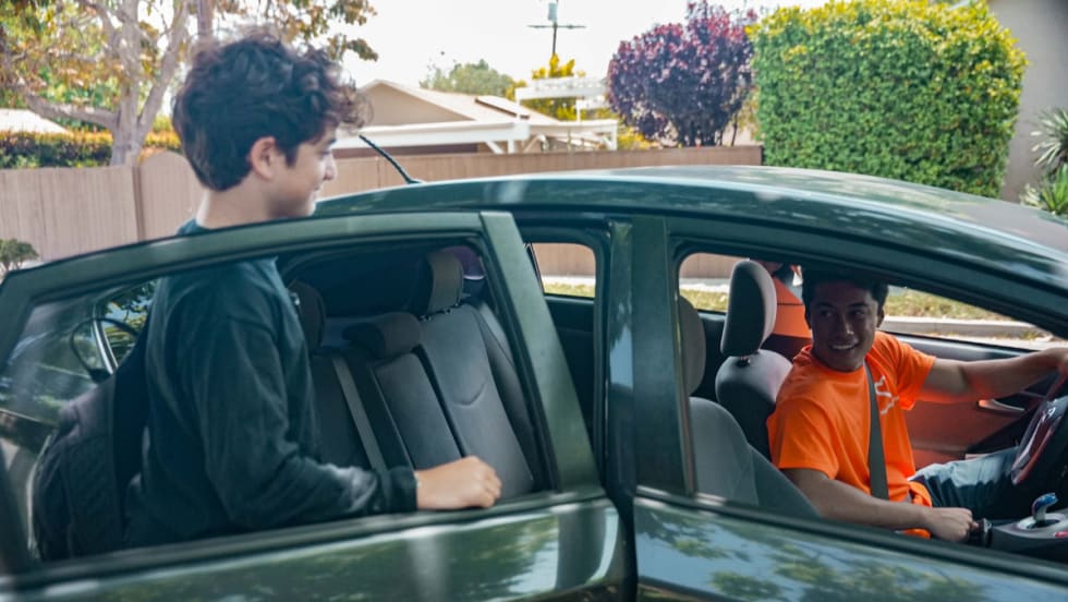 A young male student gets into the backseat of a HopSkipDrive CareDriver vehicle.