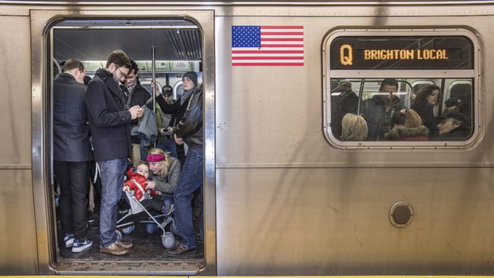 Side view of a subway car with the door open and passengers on board.