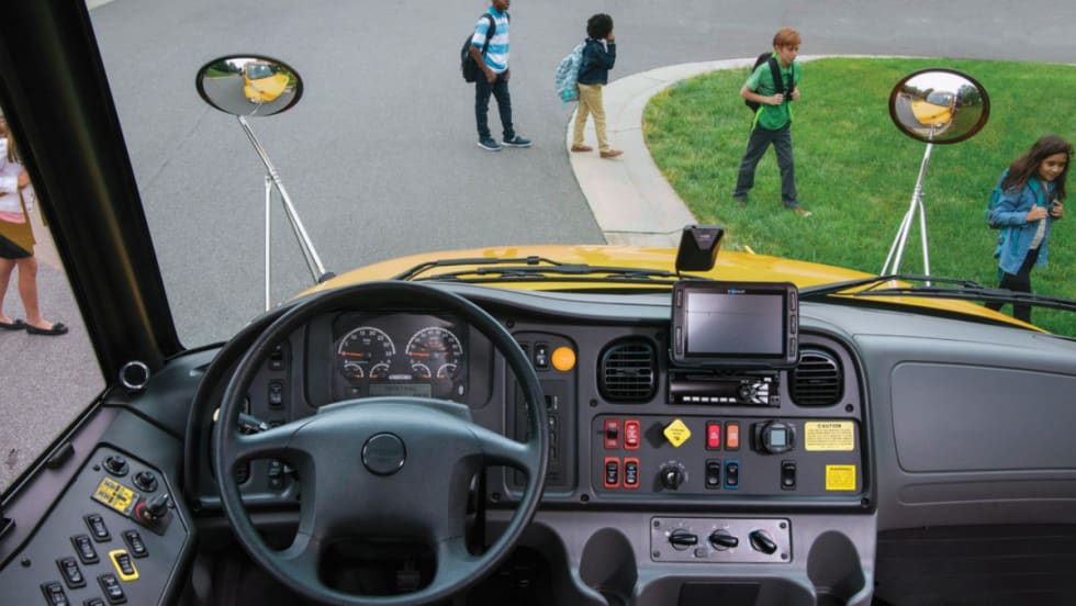 Inside view of a bus driver seat with students walking across the road.