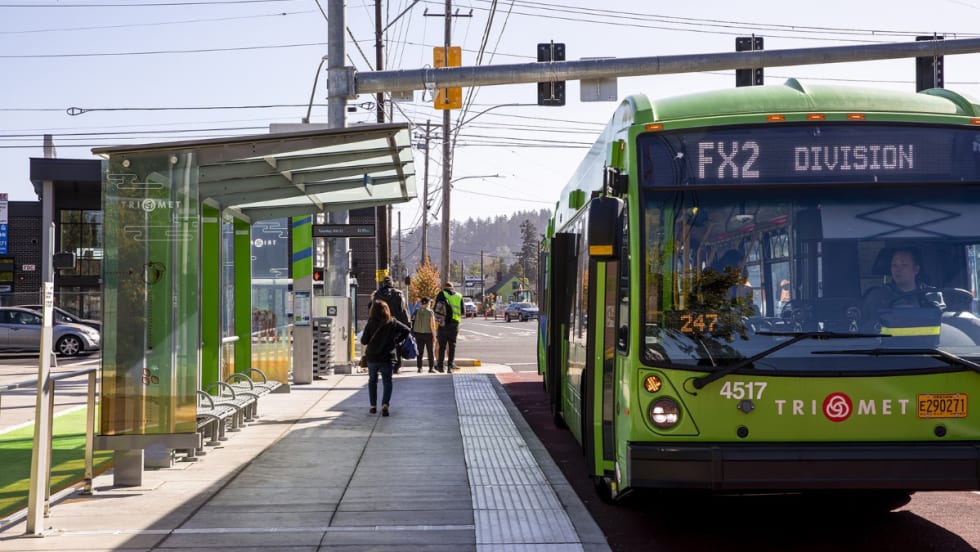 A green TriMet FX bus at a bus stop.